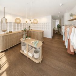 Interior de tienda de ropa con mobiliario de madera, iluminación colgante y expositores de prendas